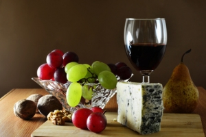Wedge of French blue veined cheese with grapes and red wine on wooden board.
